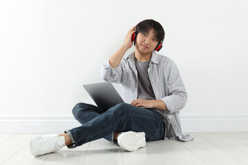 Student with headphones and laptop studying on floor indoors