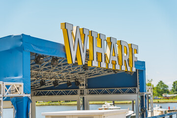 The bold Wharf sign stands out on a sunny day, marking an active waterfront event area.