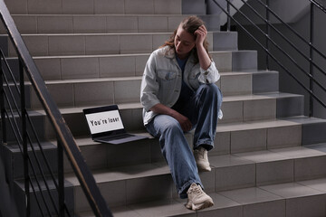 Cyber bullying. Upset teenage girl and laptop with text You Loser on stairs indoors
