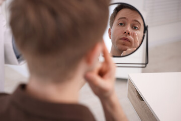 Young man putting on contact lenses near mirror in ophthalmologist office, selective focus
