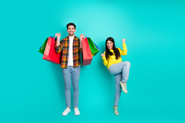 Naklejka premium Happy young couple holding shopping bags on a turquoise background celebrating and enjoying shopping