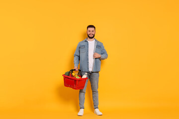 Man with shopping basket full of products on orange background