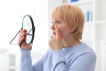Senior woman putting on contact lenses near mirror in ophthalmologist office