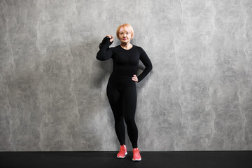 Senior woman with kettlebell near gray marble wall indoors