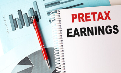Spiral notebook with text pretax earnings on top of financial charts and red pen