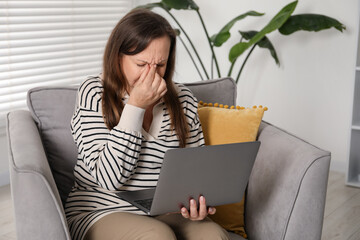 Woman with vision problem using laptop in armchair at home