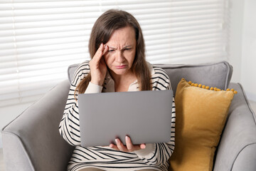Woman with vision problem using laptop in armchair at home