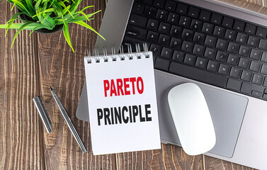 Notebook with text pareto principle on wooden desk with laptop, pen, plant and mouse