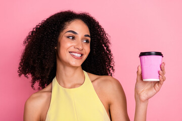 Cheerful young woman in a yellow dress holding a pink cup against a vibrant pink background,...
