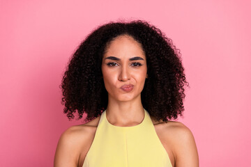 Young woman in a yellow dress making a quirky face expression against a pink background, displaying...