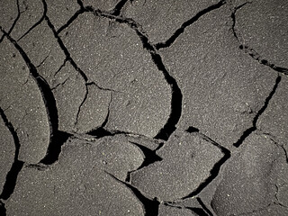 Close-up of cracked asphalt surface under strong lighting, revealing deep fractures and dry...