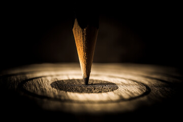 Single pencil embedded vertically into wooden surface spotlighted