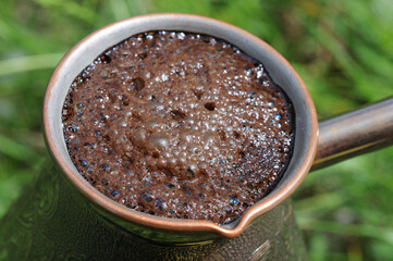 Coffee in a copper pot on a background of green grass