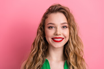 Cheerful young woman in green top posing with radiant smile and curly blonde hair on a vibrant pink...