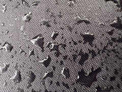 Close-up of water droplets on a waterproof fabric surface. The tightly woven texture and water beads demonstrate hydrophobic material properties, ideal for illustrating outdoor gear, moisture resistan