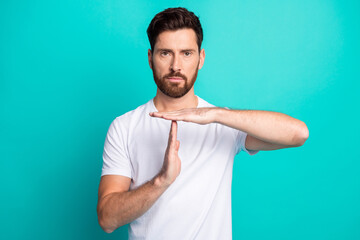 Young confident bearded man in white t-shirt making time out gesture against turquoise background