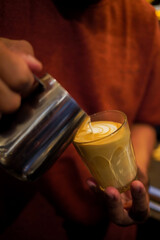 Barista making froth art on a glass of hot latte