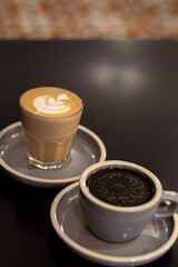 A cup of coffee and a glass of coffee latte with froth art on the counter