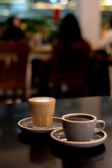 A cup of coffee and a glass of coffee latte with froth art on the table