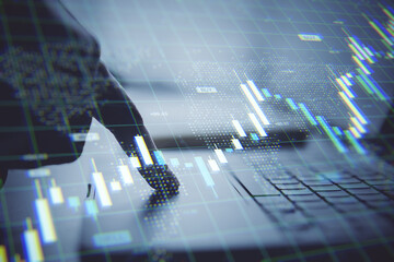Finger pressing laptop keyboard with holographic stock market chart overlay in fintech business environment on light background in office workspace.