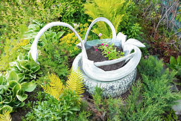 Garden decor figurine swan flowerbed with flowers in summer daytime.