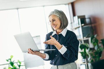 Confident mature woman in formalwear holding a laptop in a bright modern office environment