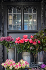 Fototapeta premium Close-up of vibrant pink and white roses and purple chrysanthemums in metal buckets by a decorative window.