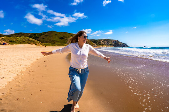 Portrait of beautiful middle aged woman enjoying walk on sandy beach in summertime. Amado beach on Algarve coast in Portugal