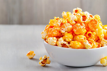 Close-up of golden caramel popcorn in a smooth white bowl on a wooden background