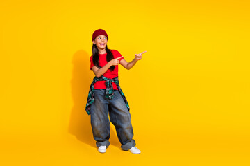 Casual preteen girl standing against yellow background with cheerful expression, trendy style, and pointing gestures