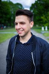A man in a polka dot shirt and black jacket smiles brightly