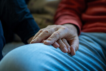 A close-up of an elderly couple holding hands tenderly, expressing support, compassion, and...