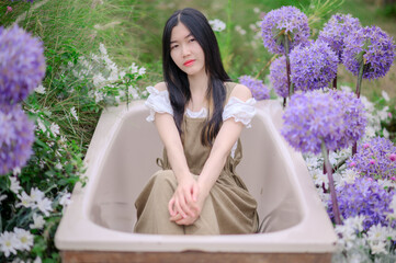 asian woman in a white blouse and brown dress sitting quietly among blooming purple allium flowers...