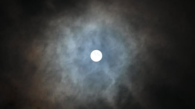 A luminous full moon emerges through soft, drifting clouds, casting an ethereal glow upon the tranquil midnight sky, evoking a sense of mystery and peace.

