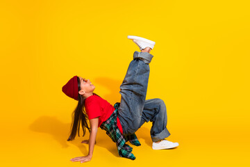 Stylish young girl doing dynamic dance pose against vibrant yellow background showcasing trendy and...