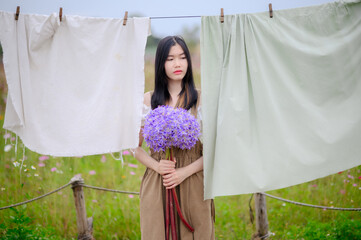 asian woman holding a large allium flower bouquet, standing quietly between hanging fabrics in a...