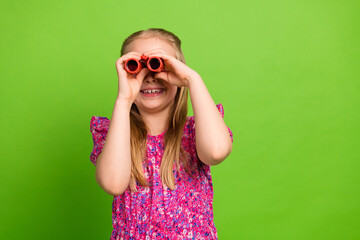 Smiling young girl looking through binoculars against a vivid green background conveying curiosity and exploration