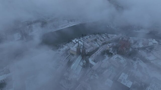 Ascending aerial winter view of Wroclaw, with snowy rooftops and clouds partially veiling the city