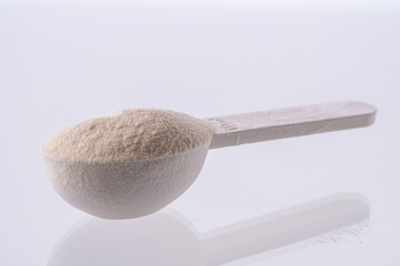 Collagen powder in a measuring spoon on a white background with reflection. A dietary supplement for beauty, health and weight loss.