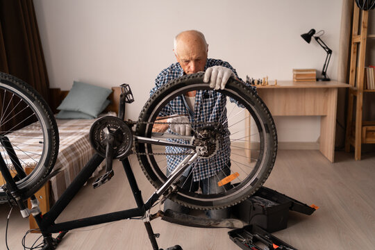 Active senior man repairing bicycle at home. cycling leisure. Retired male home mechanic with equipment for bike maintenance fixing wheel with wrench