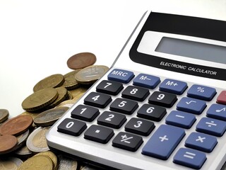 Closeup view of an electronic calculator placed next to a scattered pile of Euro coins, symbolizing budgeting, financial planning, and money management, isolated on a white background.
