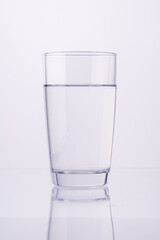 Glass of water on white background on table with reflection. Space for text. Clean, clear water in a glass glass.
