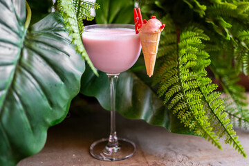 Tropical cocktail with pink drink and mini ice cream cone garnish, served in glass against lush...
