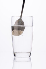 Collagen or medicinal powder is stirred with a spoon in a glass of water on a white background.