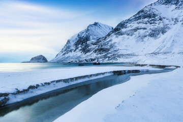 Obraz premium Beautiful snowy mountains with ice in foreground and golden sunlight at sunrise in winter in Lofoten islands, Norway. 