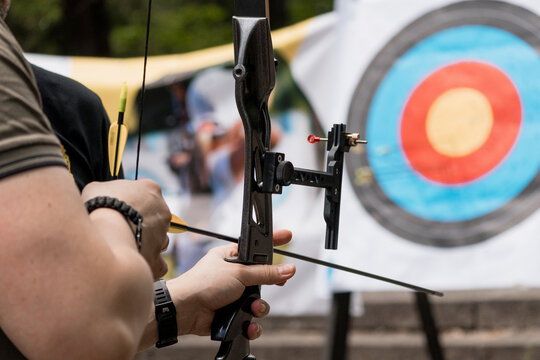 Archer Aiming Compound Bow at Target: Outdoor Archery Sport with Blue Target and Focused Male Participant, Black Equipment and Natural Light