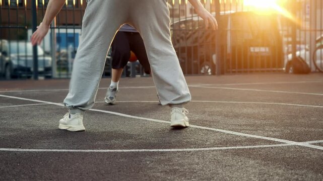 Quick-witted teen easily outmaneuvers his older bro by dribbling ball while playing basketball in park at sunset in cityscape. ball interception