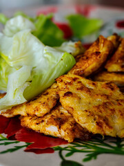 A plate of fried chicken and salad. The salad is made of lettuce and other greens. The chicken is golden brown and crispy. The plate is set on a table