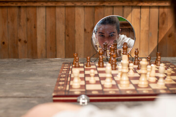 Chessboard with a chess pieces and face of a young woman reflected in a mirror	