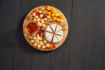 A wooden platter with a variety of cheeses and nuts, including a wedge of cheese with a piece missing